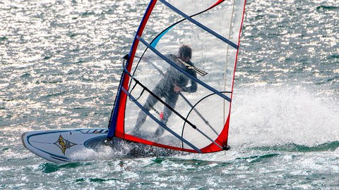 Foto: Mann steht auf Surfbrett mit Segel und surft übers Wasser