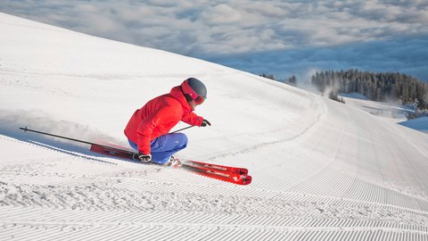 Foto Sportler mit roter Jacke fährt Abfahrtski