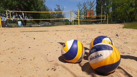 im Vordergrund liegen drei Beachvolleybälle und im Hintergrund ist eine Beachanlage