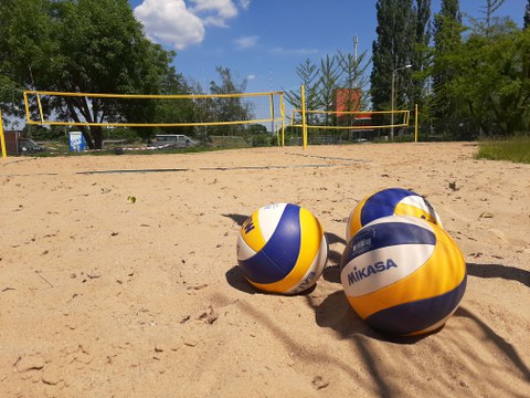 im Vordergrund liegen drei Beachvolleybälle und im Hintergrund ist eine Beachanlage