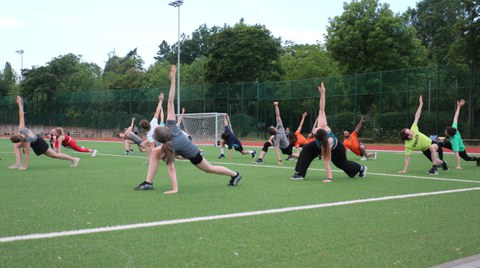 Gruppe von Menschen macht Gymnastik auf grünem Sportplatz