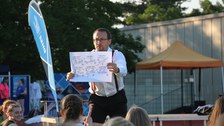 Ein Mann zeigt ein Blatt Papier mit Akrobatik-Figuren ins Publikum