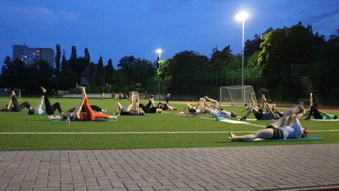 Gruppe von Menschen liegt auf dem Rasen des Sportplatzes und praktiziert Yoga