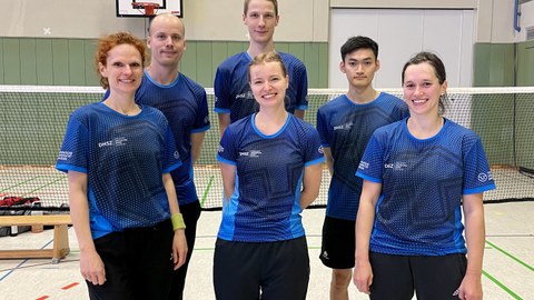 Foto 6 Sportler:innen in blauen Shirts vor einem Badminton-Netz