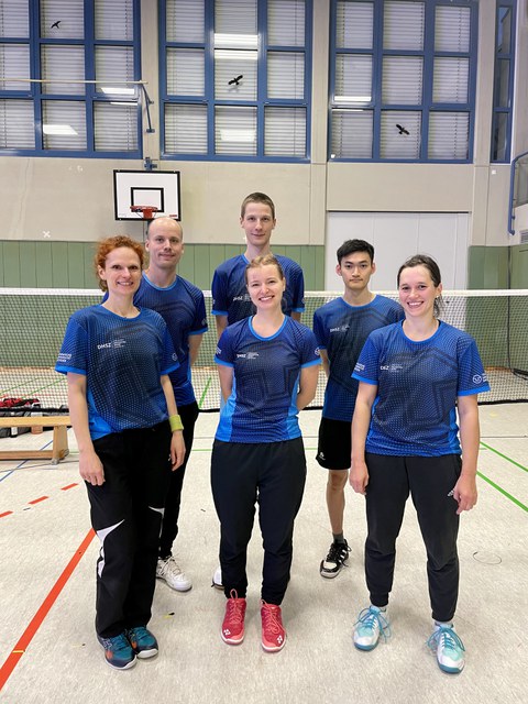 Foto 6 Sportler:innen in blauen Shirts vor einem Badminton-Netz