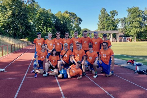 Foto Gruppe von Sportler:innen im orangefarbenen Teamshirts und blauen Hosen 