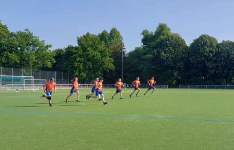 Foto Sportmannschaft in orangenen Shirts sprintet auf einem Rasenspielfeld von der Grundlinie los