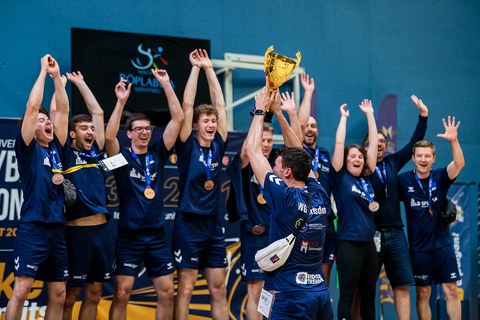 Foto: Sportler in dunkelblauen T-Shirts jubeln über einen bronzenen Pokal