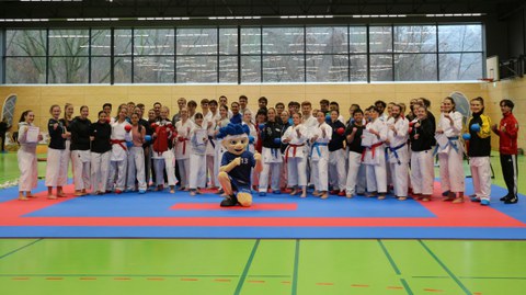 Gruppenfoto: alle Teilnehmer:innen der DHM Karate 2025 stehen hinter dem Maskottchen des DHSZ