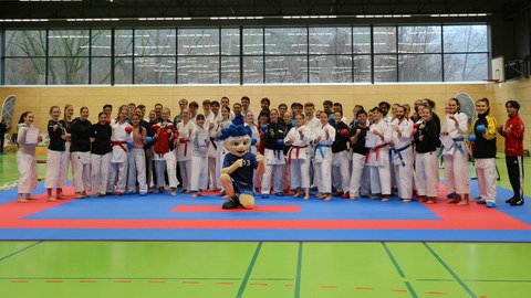 Gruppenfoto: alle Teilnehmer:innen der DHM Karate 2025 stehen hinter dem Maskottchen des DHSZ