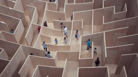 Ein Labyrinth aus Holz wird von mehreren Menschen durchschritten.