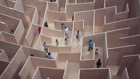 Ein Labyrinth aus Holz wird von mehreren Menschen durchschritten.