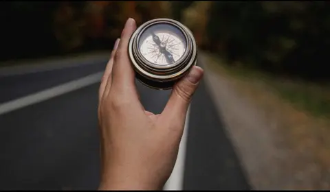 Eine Hand hält einen Kompass und lässt sich auf einer Straße leiten. 