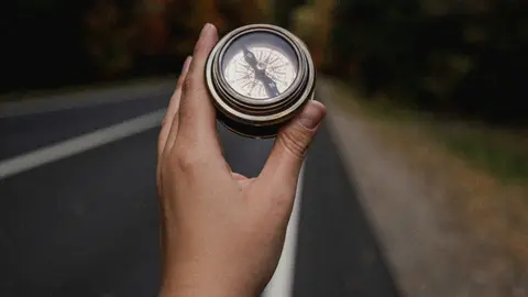 Eine Hand hält einen Kompass und lässt sich auf einer Straße leiten. 