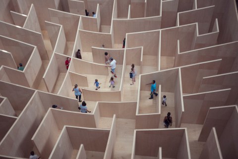 Ein Labyrinth aus Holz wird von mehreren Menschen durchschritten.