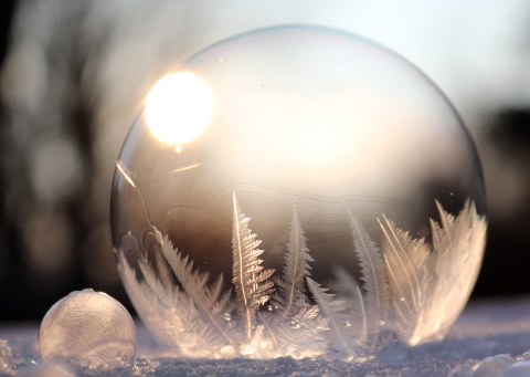 Eine Seifenblase mit Eiskristallen im Inneren. Im Hintergrund scheint die Sonne.