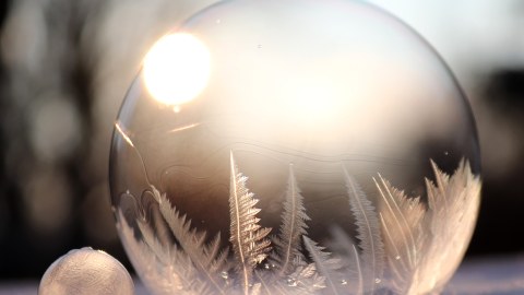 Eine Seifenblase mit Eiskristallen im Inneren. Im Hintergrund scheint die Sonne.