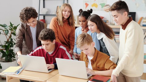 Sieben Schüler:innen arbeiten an zwei Laptops.