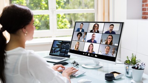 A woman at her workplace talking online in a video conference with nine colleagues.