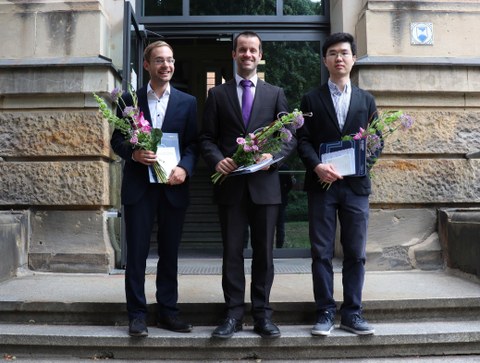 Three men stand on the steps leading up to a building holding documents and flowers. They are the recipients of the 2020 Franz Stolze Prize.