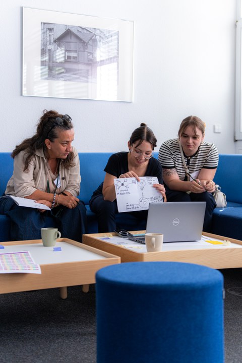 Drei Frauen sitzen vor einem Laptop und arbeiten