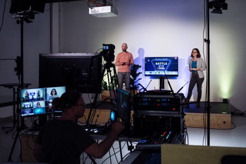 Blick ins Studio, Vordergrund: Kameratechnik, Hintergrund: 2 Personen auf einer Bühne