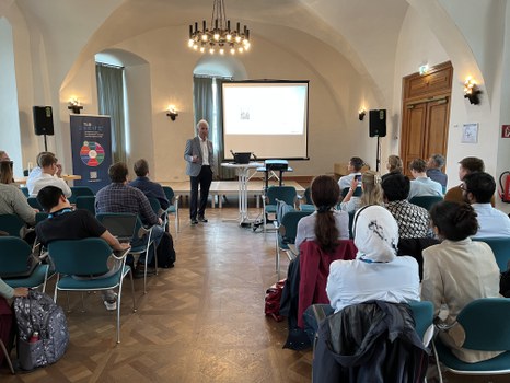 Participants in the audience, professor presenting in front of a projection screen