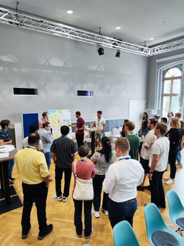 eine Gruppe präsentiert ihr Board, andere Teilnehmende stehen um Board und hören gespannt zu
