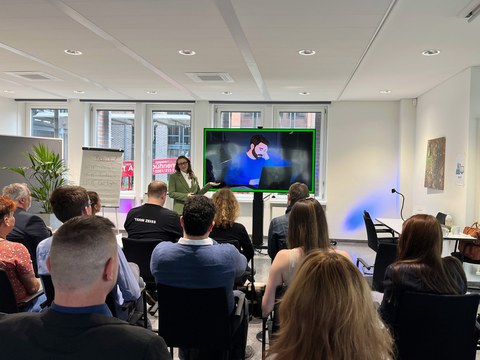 One person is giving a presentation in front of a screen; others are sitting in the audience