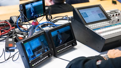Das Foto zeigt die Kabel und die Bildschirme eines Technikers, der einen Vortrag während einer Tagung online streamt.