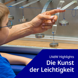 Foto: Kind mit Brille beobachtet eine Hand, die an einem Pendel aus Metallgewichten zieht