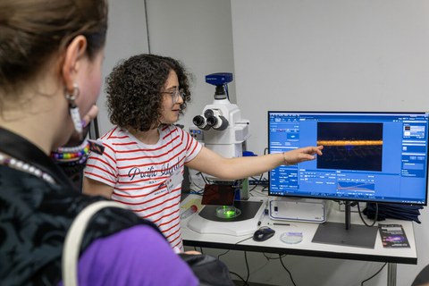 Foto von zwei Personen, die auf einen Monitor schauen. Die eine Person zeigt der anderen etwas auf dem Monitor. 