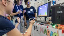 Foto von mehreren Personen, die ein Computerspiel bei der Langen Nacht der Wissenschaften spielen. Die Personen haben Elektroden auf den Armen und Händen und steuern damit das Spiel. 