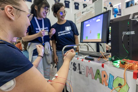 Foto von mehreren Personen, die ein Computerspiel bei der Langen Nacht der Wissenschaften spielen. Die Personen haben Elektroden auf den Armen und Händen und steuern damit das Spiel. 