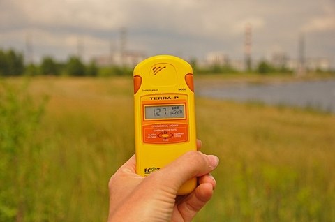 Hand mit einem Messgerät für radioaktive Strahlung vor einem grünen Feld