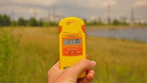 Hand mit einem Messgerät für radioaktive Strahlung vor einem grünen Feld