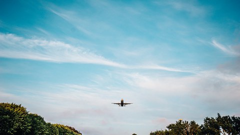 Das Foto zeigt ein Flugzeug im Landeanflug. Am unteren Bildrand stehen einige Bäume