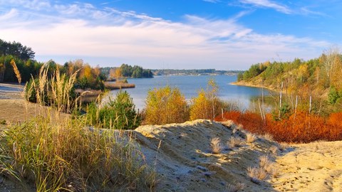 Das Foto zeigt eine Dünenlandschaft. In deren Mitte befindet sich ein Badesee.