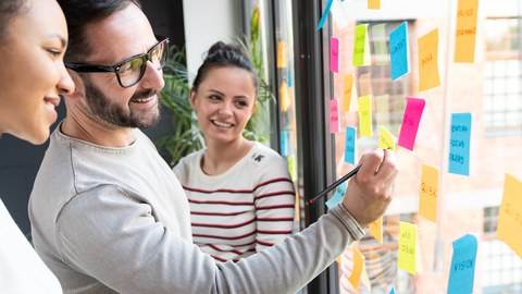 Zwei Frauen und ein Mann verwenden Klebezettel für Brainstorming