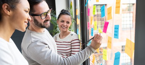 Zwei Frauen und ein Mann verwenden Klebezettel für Brainstorming