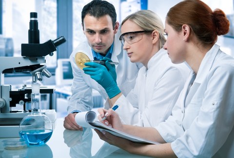 Two female and one male scientist examining a Petri dish in the laboratory.