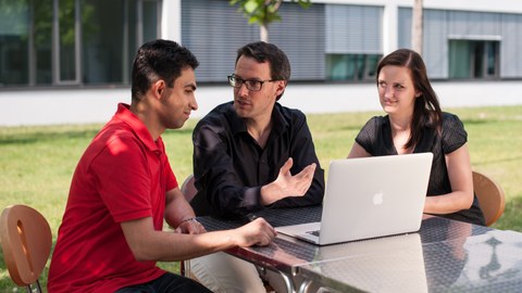 Three scientists discuss in front of a laptop computer