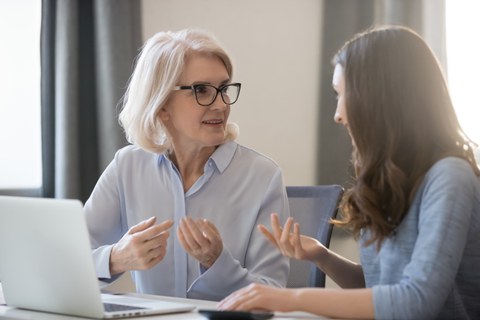 Two persons read as female. Older person on the left in conversation with younger person on the right at a table.