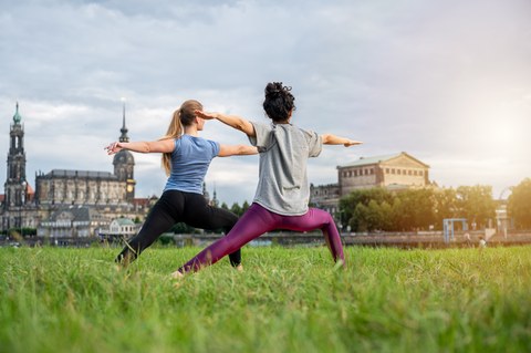 Zwei Frauen stehen in der Yogaposition "Krieger" am Elbufer