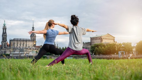 Zwei Frauen stehen in der Yogaposition "Krieger" am Elbufer