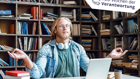 Junger blonder Mann mit brille sitzt in Meditationsposition vor seinem Laptop in der Bibliothek
