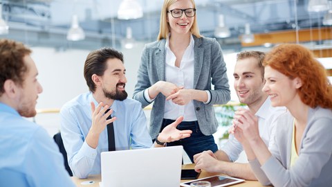 Personen sitzen um einen Tisch mit Laptop und unterhalten sich