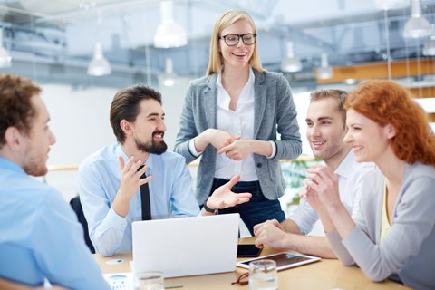 Personen sitzen um einen Tisch mit Laptop und unterhalten sich