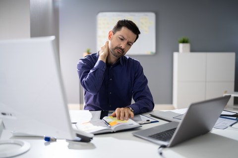 Photo of person at desk holding neck 