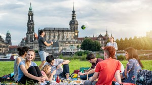 Foto: Gruppe von Studierenden an der Elbe. Sie spielen Volleyball und sitzen plaudernd auf der Wiese.